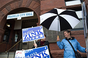 two women campaign for Olivia Zink with umbrellas and election signs