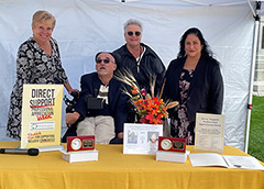 4 people together behind a table with a yellow table cloth and a photo with 2 awards on it.
