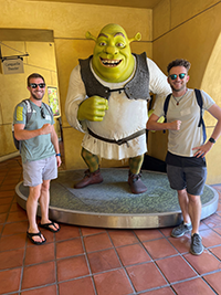 two young men pose in front of a Shrek statue